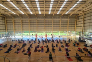 Participantes de un encuentro de yoga en el microestadio municipal de Don Torcuato, ejecutando diversas posturas sobre sus colchonetas en un amplio espacio cubierto.