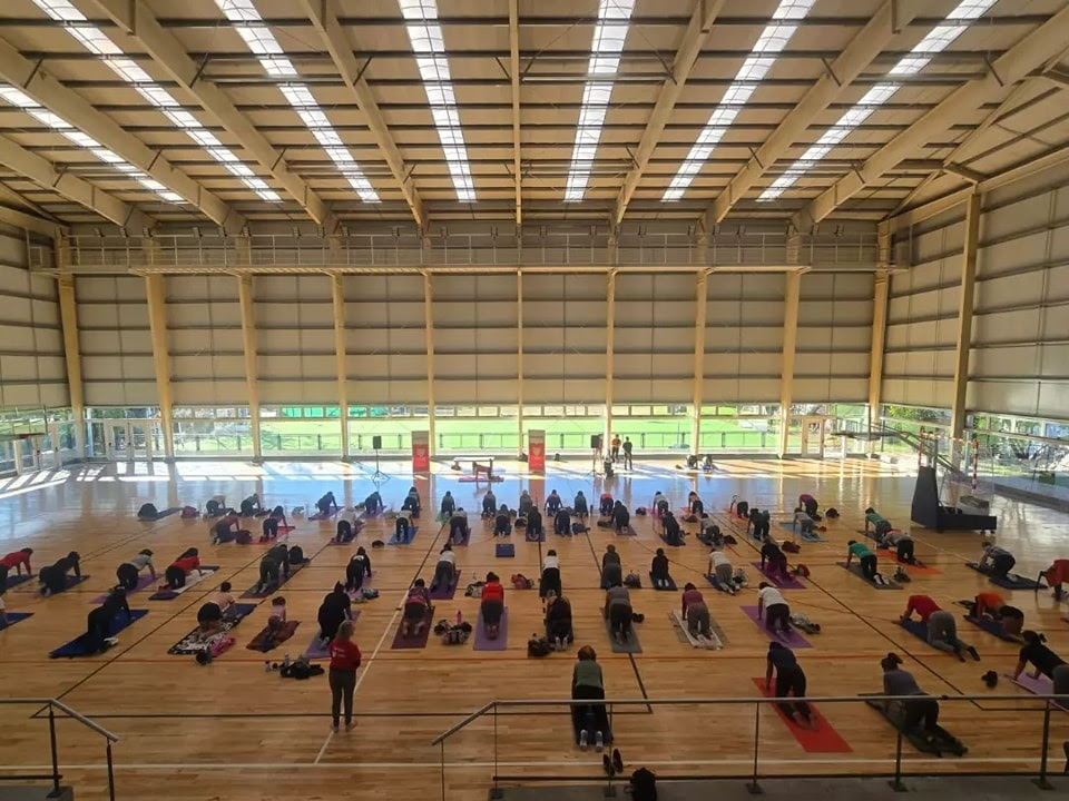 Participantes de un encuentro de yoga en el microestadio municipal de Don Torcuato, ejecutando diversas posturas sobre sus colchonetas en un amplio espacio cubierto.