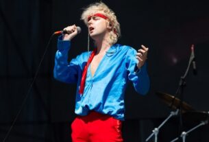 Benito Cerati, músico y cantante, en pleno espectáculo, luciendo una camisa azul y pantalones rojos, mientras canta en el escenario.