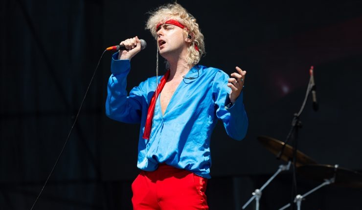 Benito Cerati, músico y cantante, en pleno espectáculo, luciendo una camisa azul y pantalones rojos, mientras canta en el escenario.