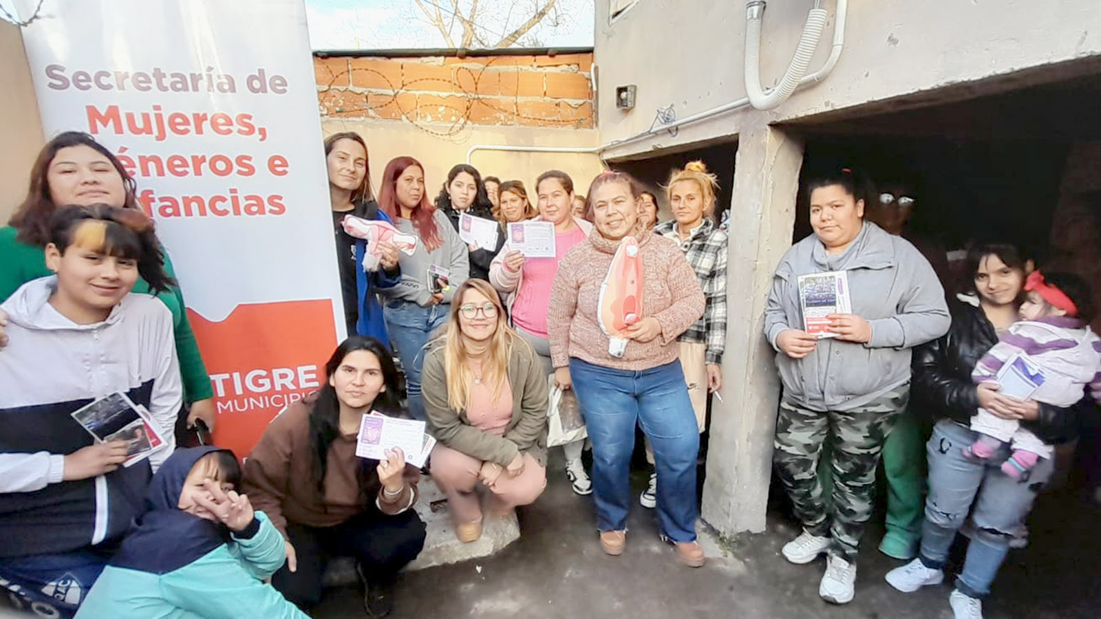 Un grupo de mujeres y niñas participan en el programa "Tigre se COPA" en el barrio Almirante Brown, sosteniendo material informativo y copas menstruales.