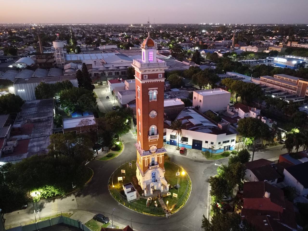 Vista aérea de la Torre Ader en Vicente López al atardecer, mostrando la torre iluminada y rodeada de edificios y calles.