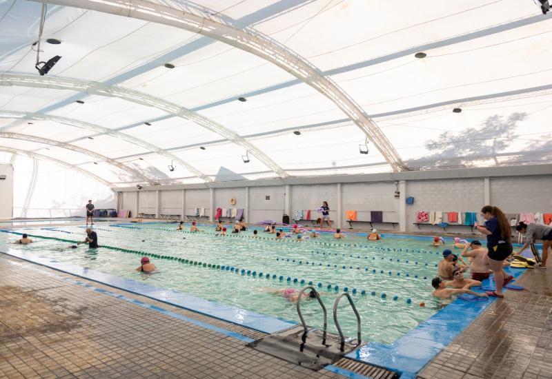 Piscina cubierta del Campo de Deportes Nº4 en Martínez, San Isidro, con personas de distintas edades practicando natación y gimnasia acuática tras las remodelaciones realizadas por el municipio.