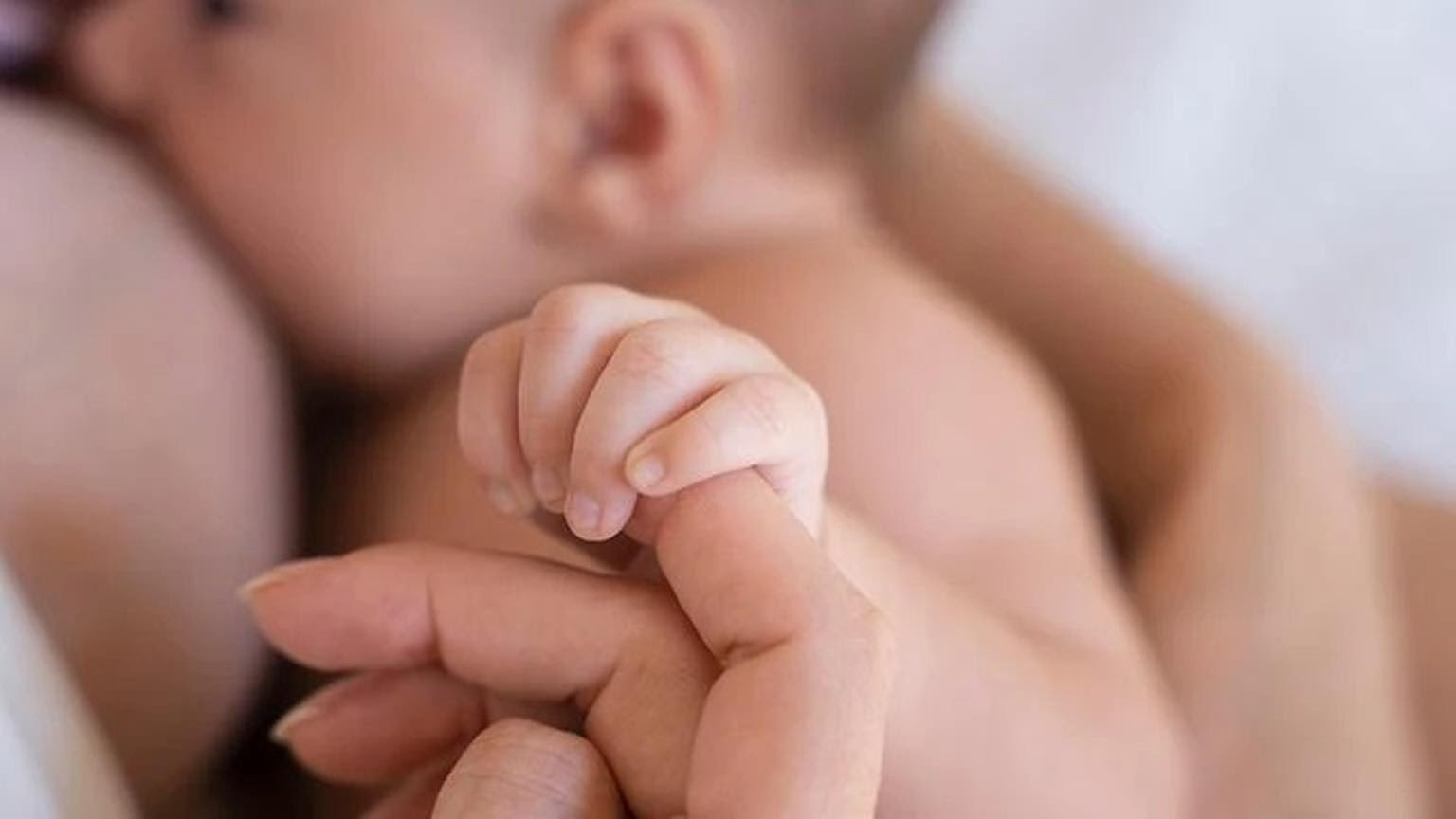 Un bebé lactando mientras agarra el dedo de su madre, destacando el vínculo cercano y la importancia del amamantamiento.