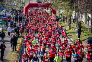 Gran cantidad de corredores participando en la Carrera Comunidad de Tigre, todos con camisetas rojas, al inicio de la carrera bajo un arco inflable rojo en El Talar.