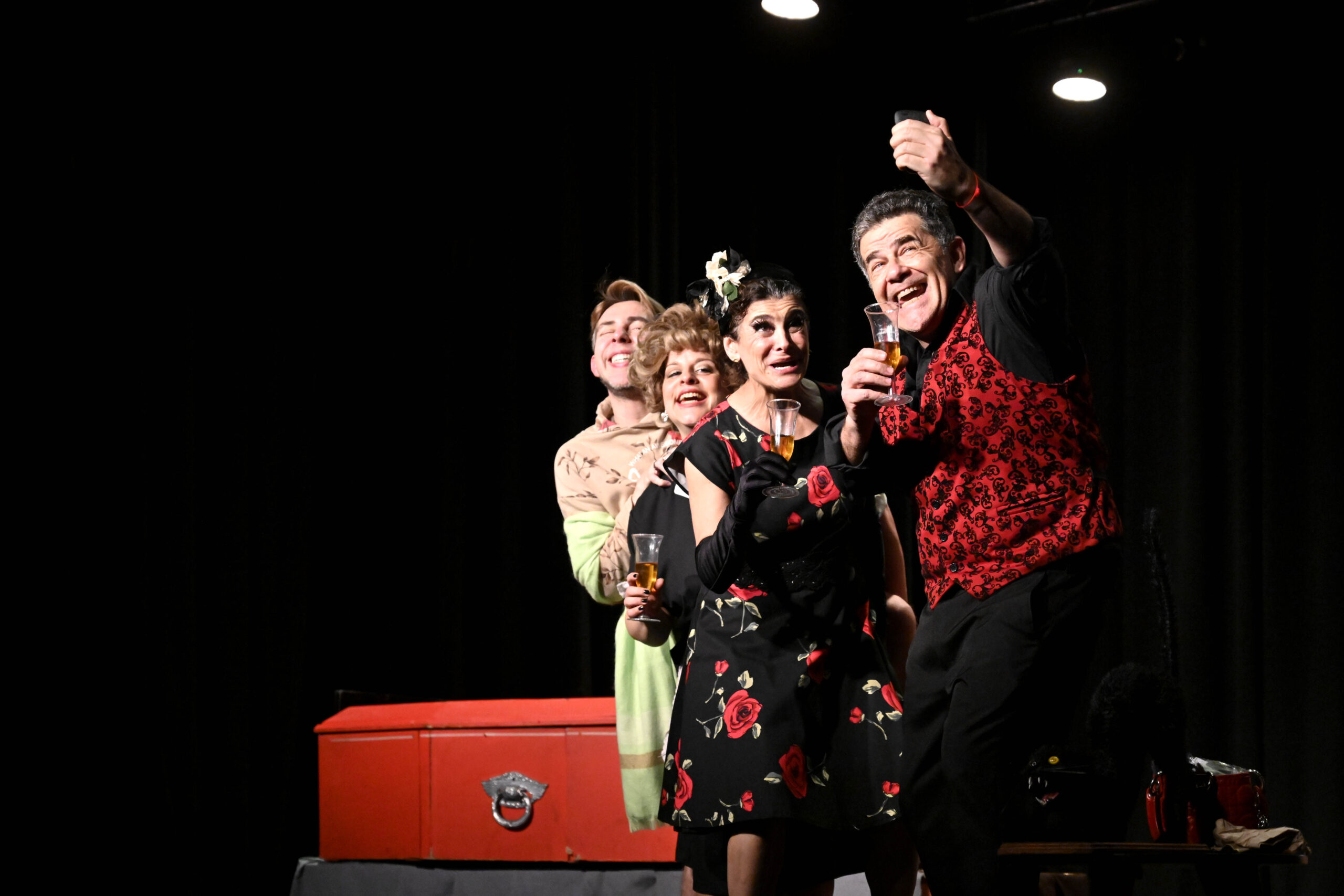 Los actores Julián Weich, Fabián Arenillas, Celeste Campos, Nicolás Maiques y Alejandra Majluf en escena, vestidos con atuendos llamativos, brindando con copas, en una representación de la obra "Velorio a la carta" en el Teatro de General Pacheco.