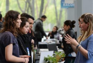 Grupo de jóvenes hablando con una expositora en uno de los stands de Expo Joven, en un ambiente de feria con diversas personas y actividades en segundo plano.